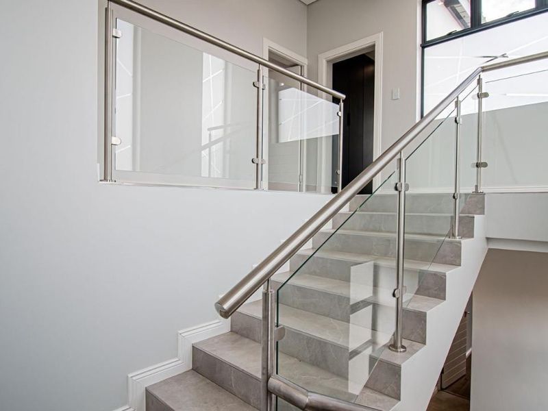 Modern staircase featuring tiled treads, a sleek glass balustrade, and a stainless steel handrail in a bright, contemporary hallway.