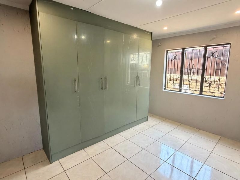 A bedroom featuring tiled flooring, recessed downlighting, and floor-to-ceiling built-in cupboards with a window fitted with security bars.