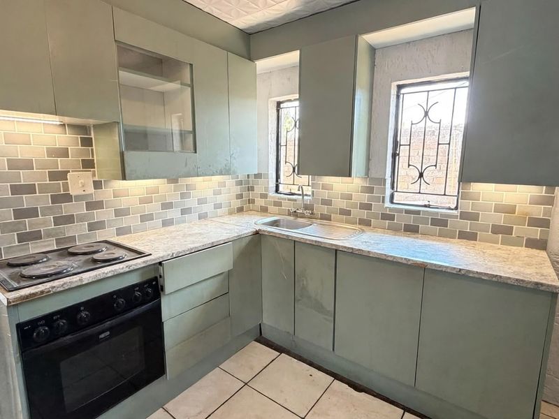 A functional kitchen featuring sage green cabinetry, subway tile backsplash, built-in oven and hob, and ample counter space with security-fitted windows.