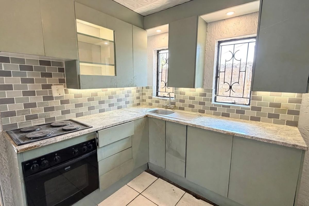 A compact kitchen featuring sage green cabinetry, subway tile backsplash, stone-look laminate countertops, and integrated electric cooking appliances.