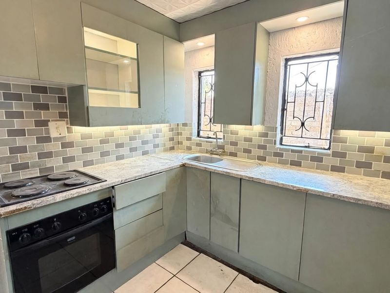 A compact kitchen featuring sage green cabinetry, subway tile backsplash, stone-look laminate countertops, and integrated electric cooking appliances.