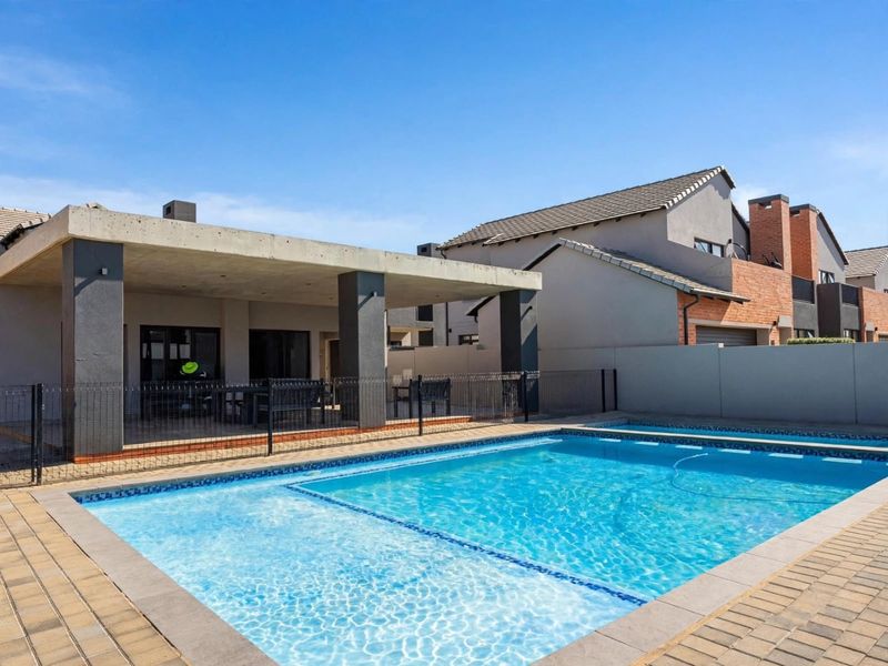 A well-maintained swimming pool area featuring a paved surround and a spacious covered patio with a modern concrete roof structure.