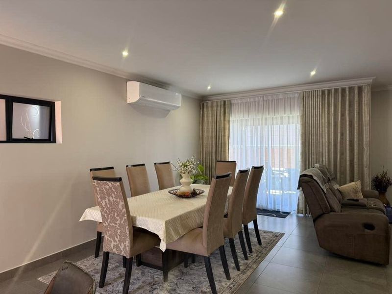 A well-maintained open-plan living and dining area featuring tiled floors, recessed lighting, a wall-mounted air conditioner, and large sliding doors with floor-to-ceiling curtains.