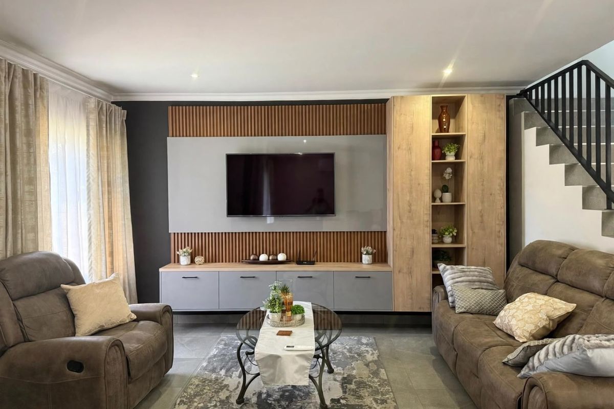 Modern living room featuring a custom built-in media unit with timber slat detailing, integrated shelving, and a sleek staircase with a contemporary metal balustrade.