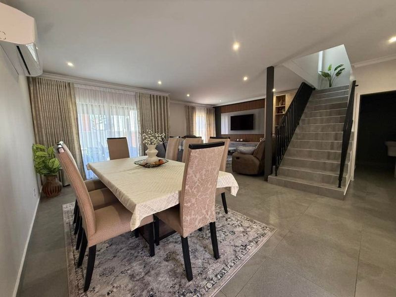 Spacious open-plan living and dining area featuring modern tiled flooring, recessed lighting, and a contemporary staircase with a sleek metal balustrade.