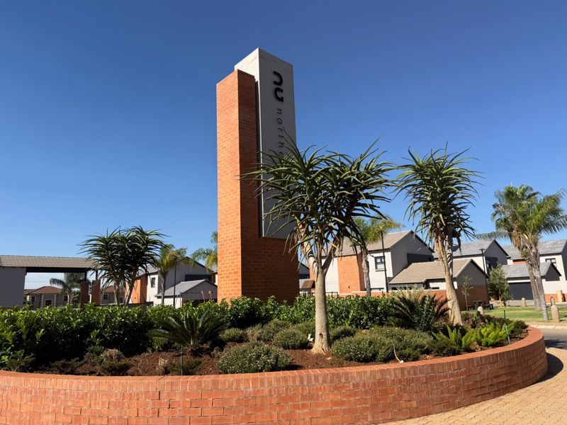 Entrance to the residential estate featuring a modern brick signage pillar, landscaped garden beds, and paved driveway access.