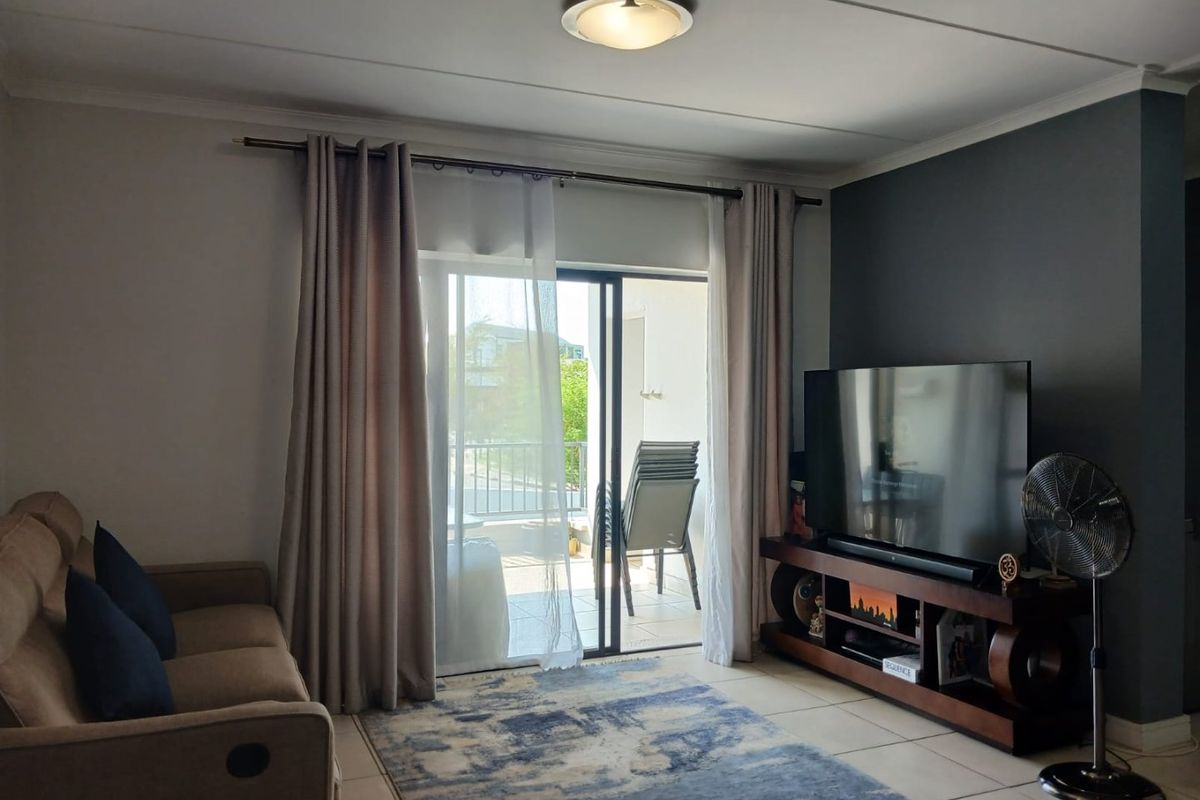 A well-maintained living room featuring tiled flooring, a dark accent wall, and a sliding glass door providing access to an outdoor balcony.