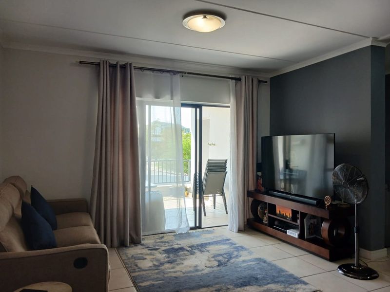 A well-maintained living room featuring tiled flooring, a dark accent wall, and a sliding glass door providing access to an outdoor balcony.