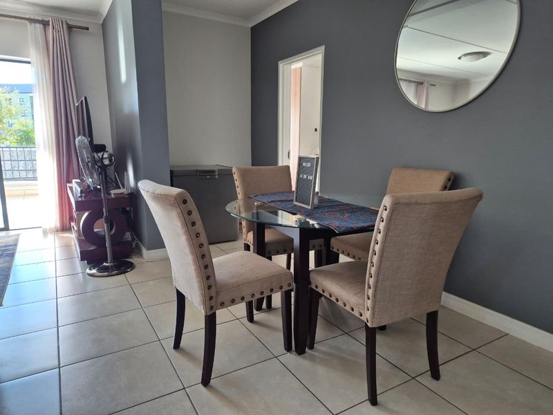 A well-lit dining area featuring neutral tiled flooring and direct access to an outdoor balcony through a sliding glass door.