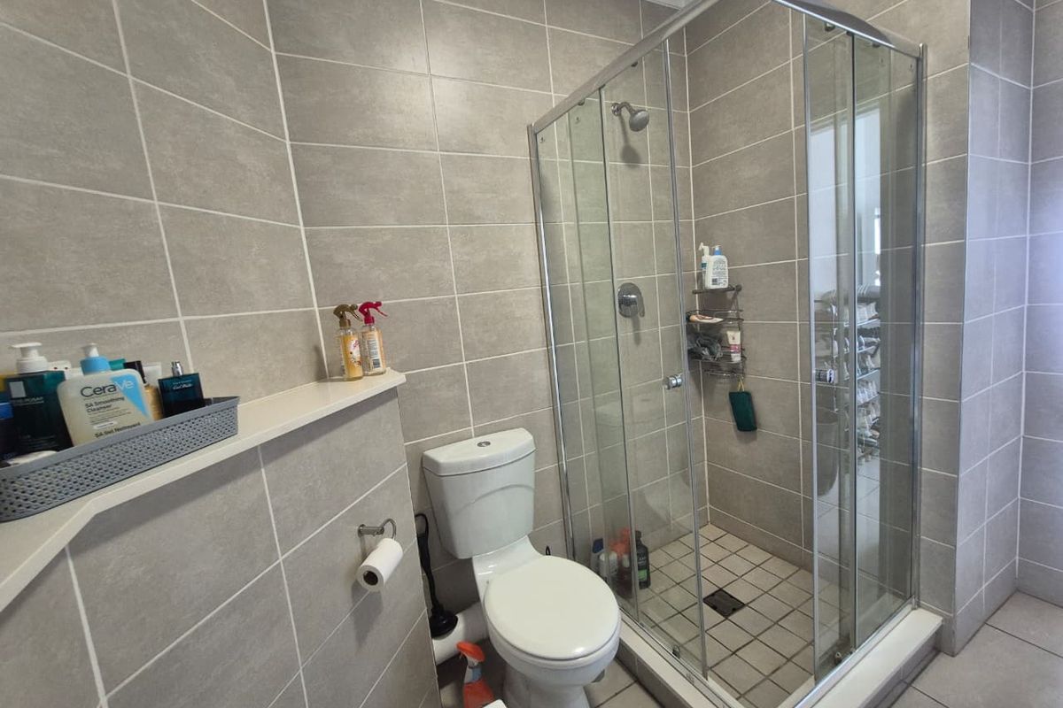 A modern bathroom featuring a glass-enclosed shower, a standard toilet, and neutral grey wall and floor tiling.