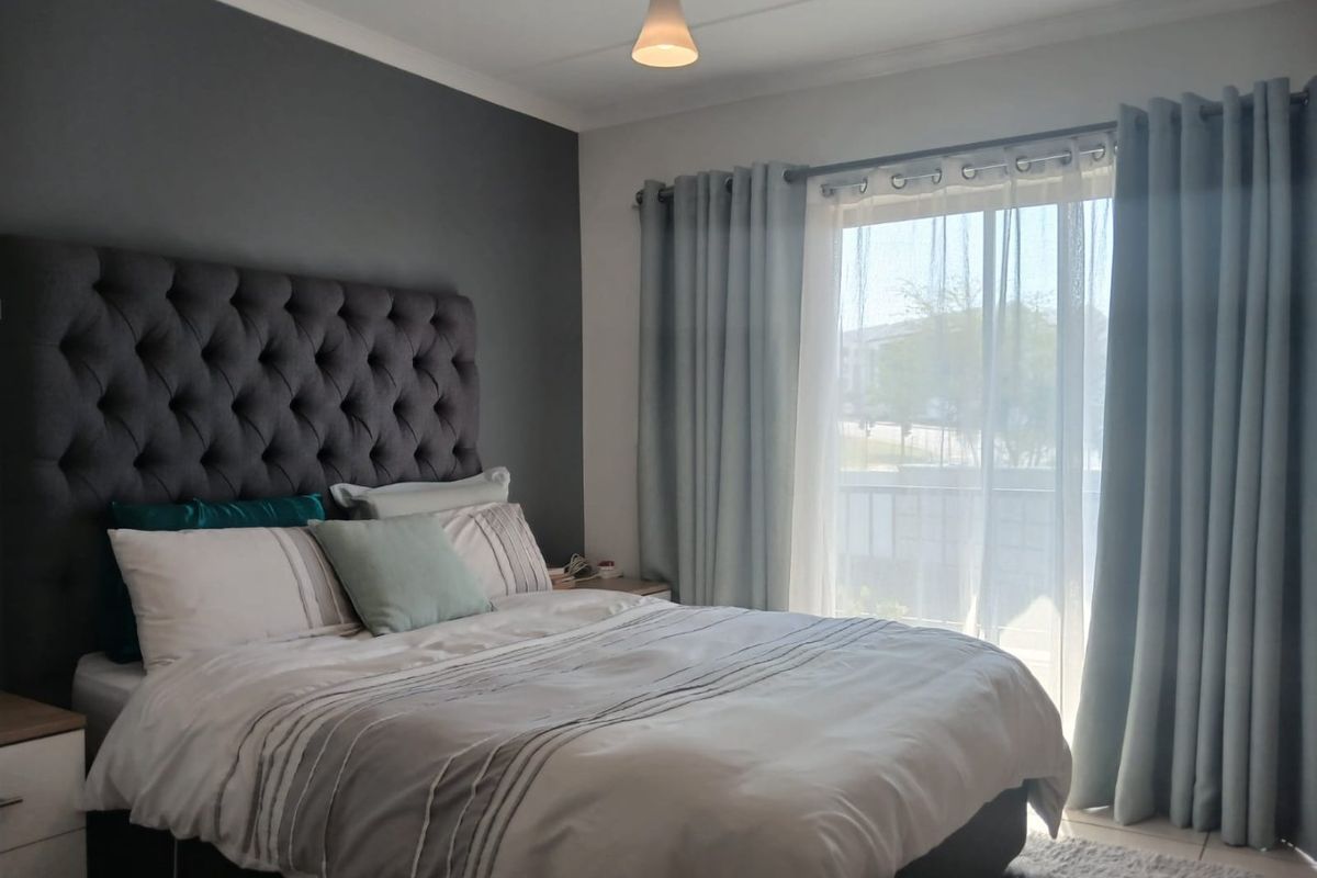 A well-lit bedroom featuring tiled flooring, a feature wall, and a sliding glass door providing access to an outdoor area.