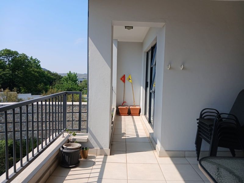 A spacious covered balcony featuring tiled flooring, a metal safety balustrade, and direct access to the interior through a sliding glass door.