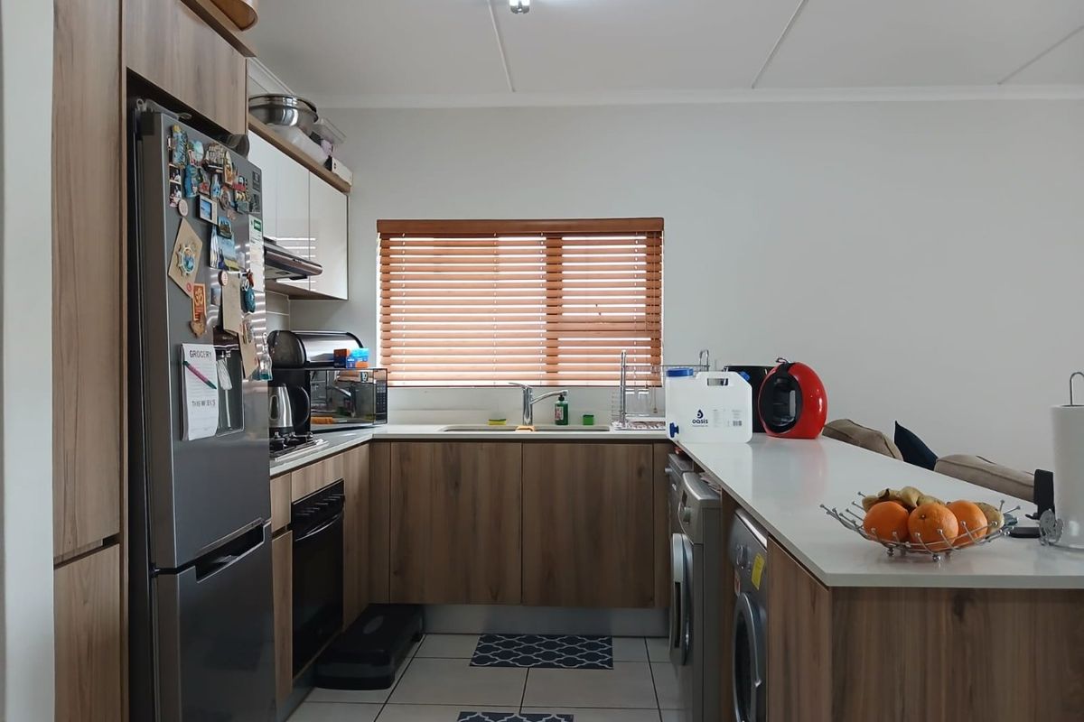 A functional kitchen featuring modern wood-look cabinetry, integrated appliances, tiled flooring, and a breakfast bar counter, providing a practical and well-organized cooking space.