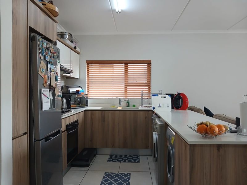 A functional kitchen featuring modern wood-look cabinetry, integrated appliances, tiled flooring, and a breakfast bar counter, providing a practical and well-organized cooking space.