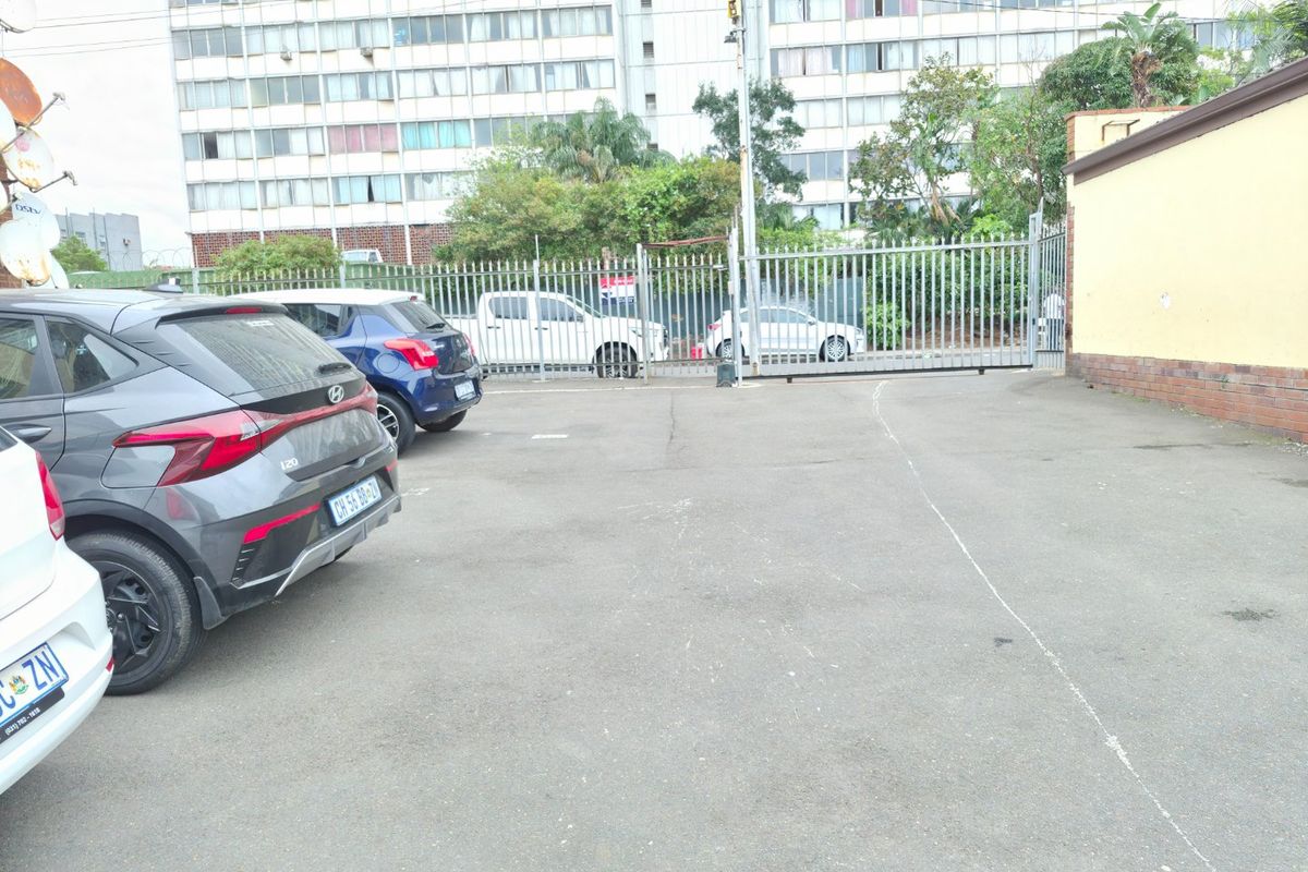 A paved parking area featuring a secure metal gate and perimeter fencing, providing access to the apartment complex.