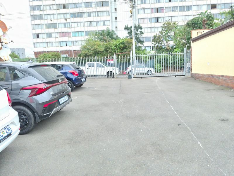 A paved parking area featuring a secure metal gate and perimeter fencing, providing access to the apartment complex.