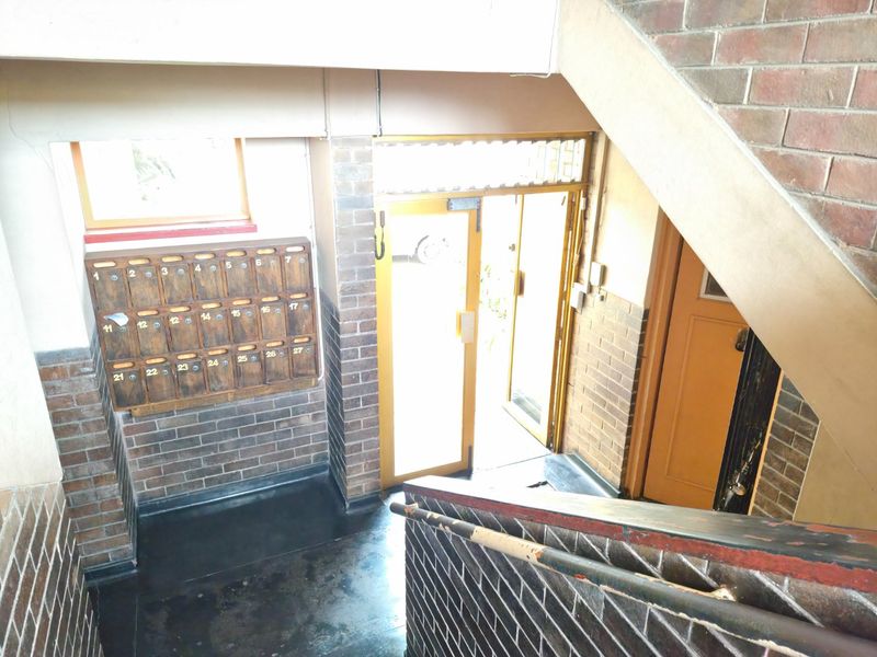 Communal apartment building entrance foyer featuring brick walls, a staircase with a metal handrail, and a bank of mailboxes.