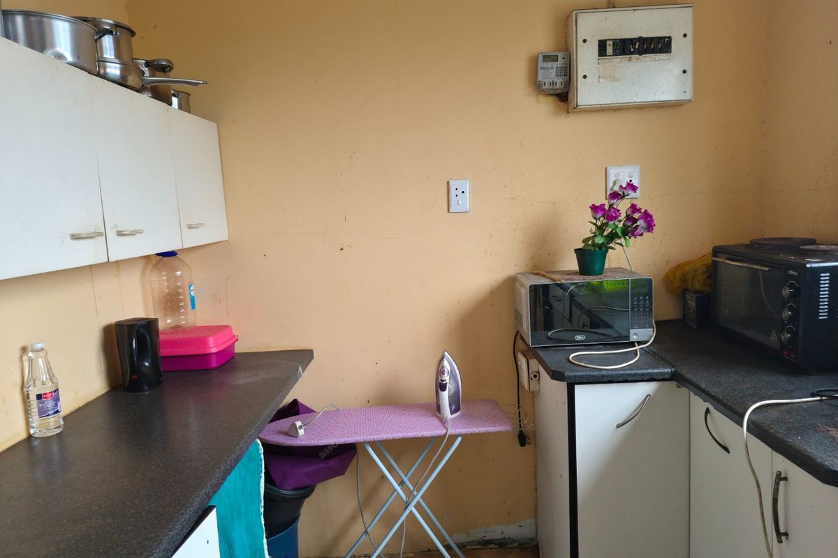 A functional kitchen area featuring built-in cabinetry, laminate countertops, and an integrated electrical distribution board, requiring cosmetic updates to improve its overall condition.