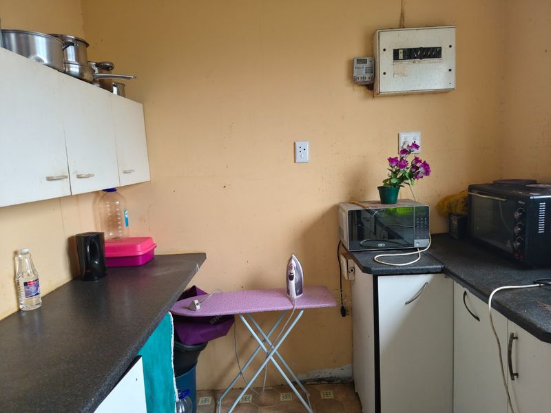 A functional kitchen area featuring built-in cabinetry, laminate countertops, and an integrated electrical distribution board, requiring cosmetic updates to improve its overall condition.