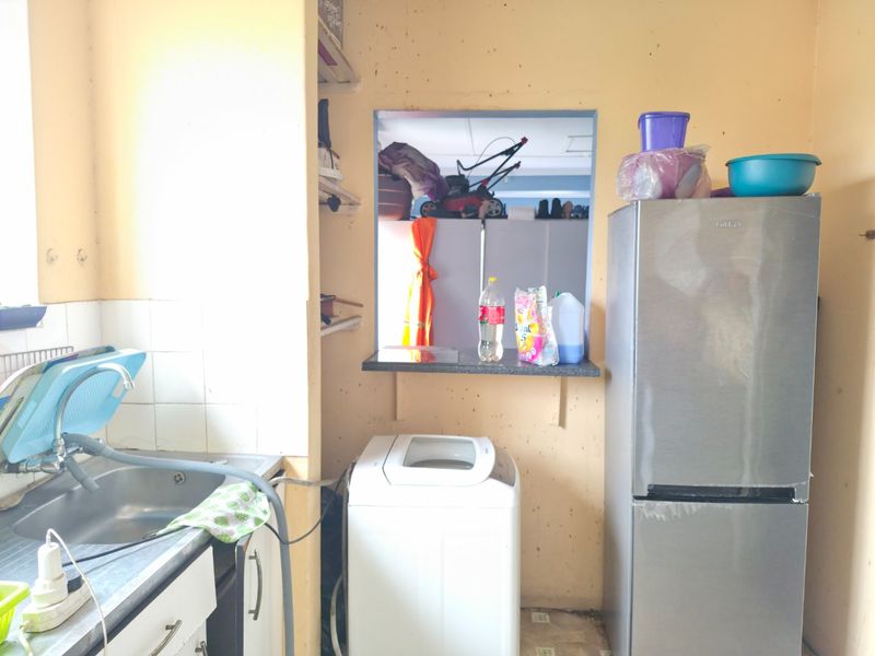A functional laundry area featuring a stainless steel sink, tiled splashback, and a pass-through window, requiring cosmetic updates to the wall finishes.