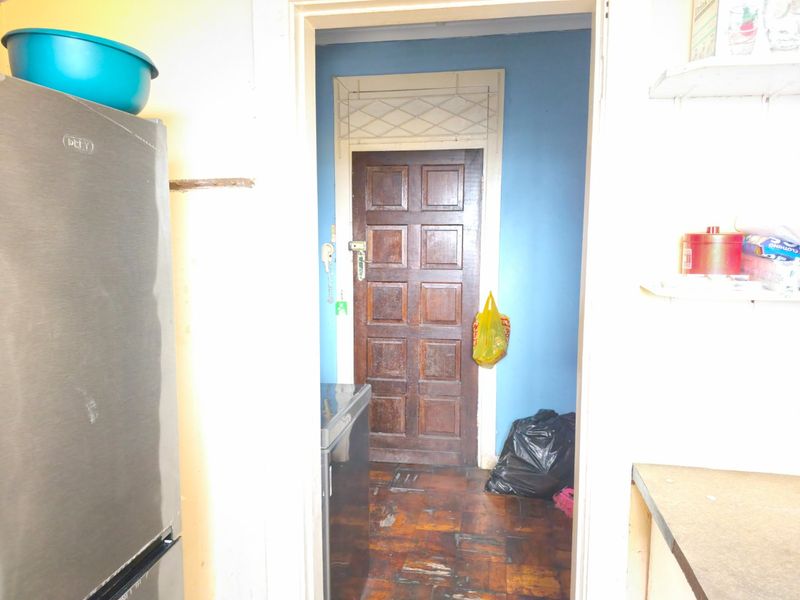 A narrow hallway featuring traditional parquet flooring and a solid wooden panel door, requiring cosmetic updates to improve the overall aesthetic.