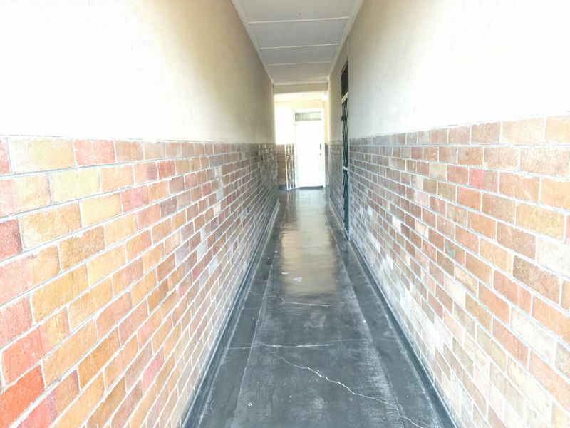 A narrow apartment hallway featuring exposed brick wall accents and tiled flooring, leading towards an entrance door.