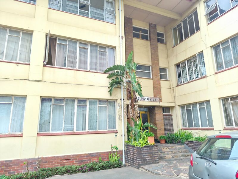 Front elevation of a multi-story apartment building featuring a brick and plaster facade with steel-framed windows and a stone-paved entrance area.