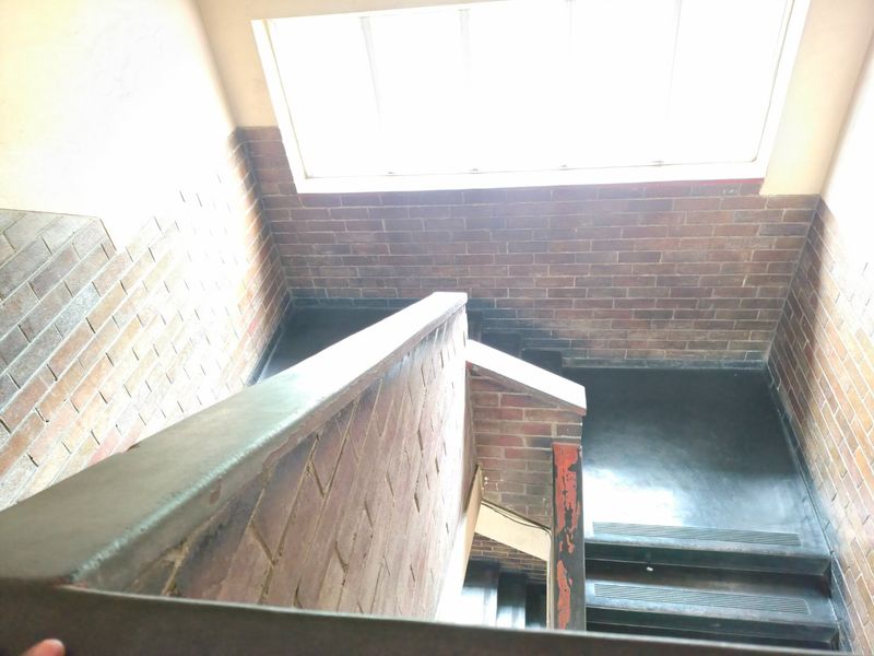 A stairwell featuring exposed brick walls, a large window for natural light, and a functional staircase with a handrail.