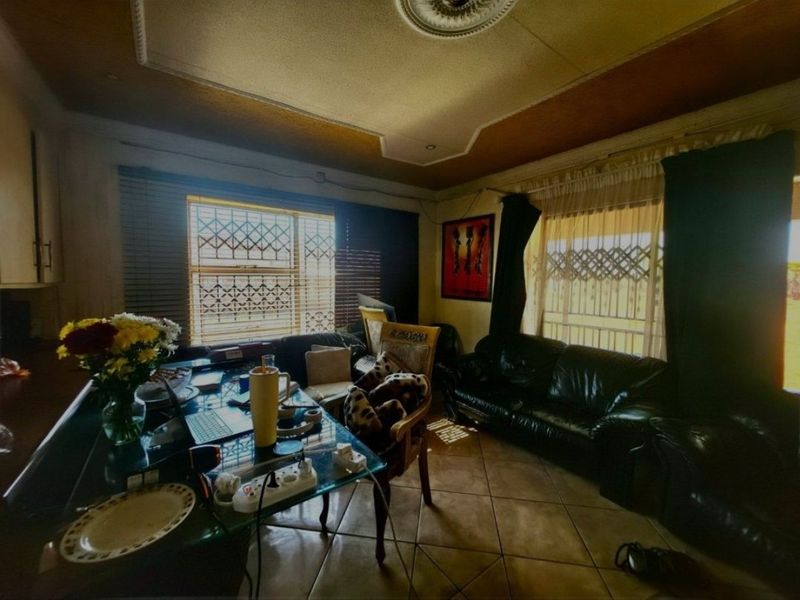 A living room featuring tiled flooring, decorative ceiling details, and security burglar bars on the windows, offering a dated space ready for modernization.