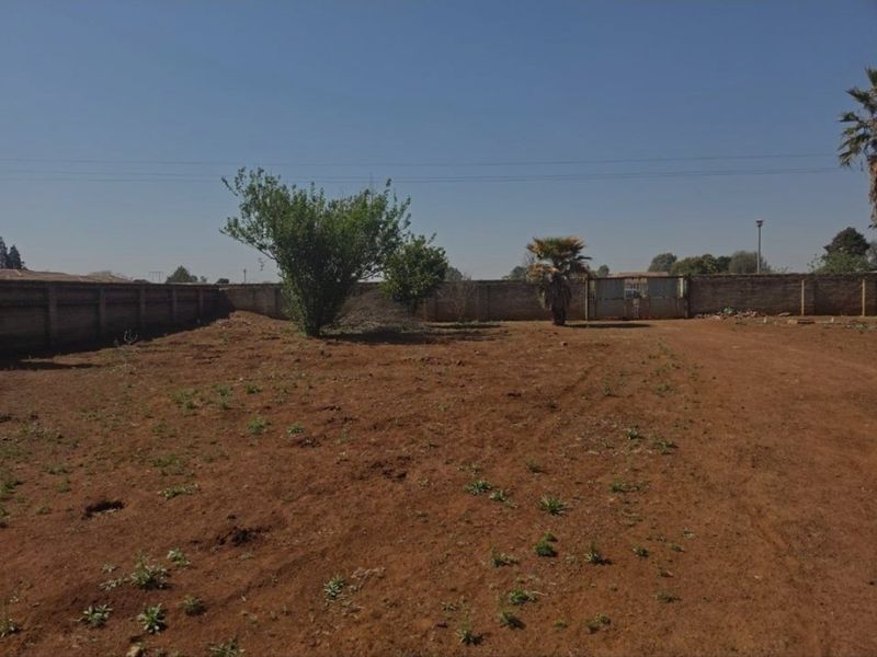 A large, undeveloped plot of land enclosed by a perimeter brick wall and featuring a metal access gate.