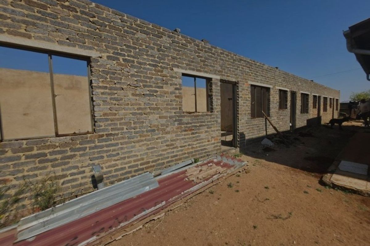 An unfinished residential structure showing exposed brick walls and open window and door frames, requiring significant completion and finishing work.