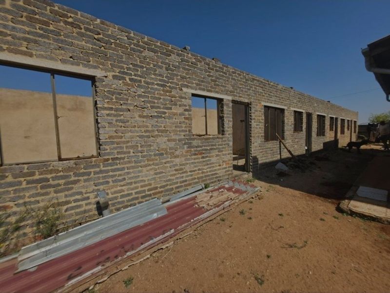 An unfinished residential structure showing exposed brick walls and open window and door frames, requiring significant completion and finishing work.