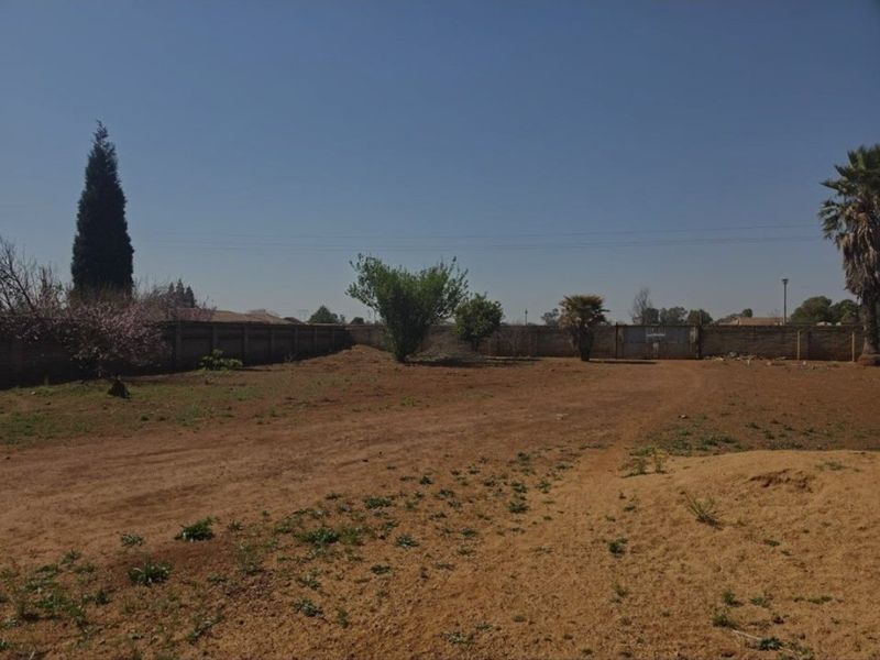 A large, undeveloped plot of land featuring a perimeter wall and a metal gate, offering significant potential for landscaping or future development.