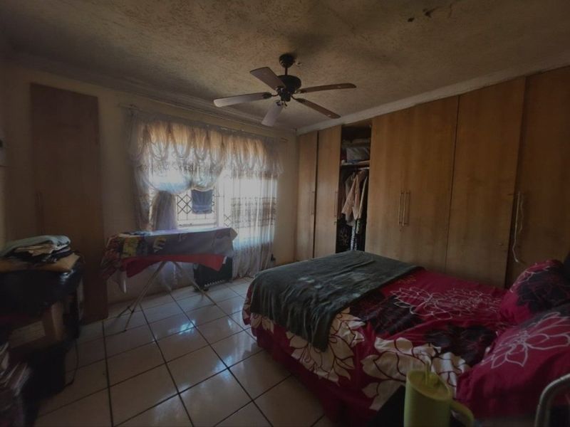 A bedroom featuring built-in cupboards, tiled flooring, and a ceiling fan. The room requires cosmetic updates, particularly to the ceiling finish.