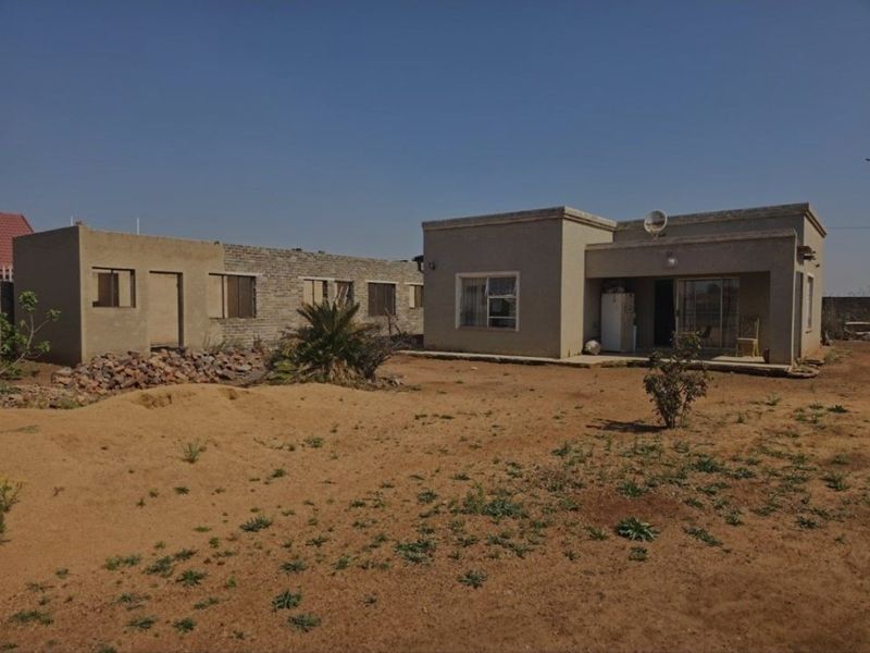Rear view of a single-story house featuring a covered patio, sliding doors, and an expansive, unlandscaped yard with unfinished brickwork sections.