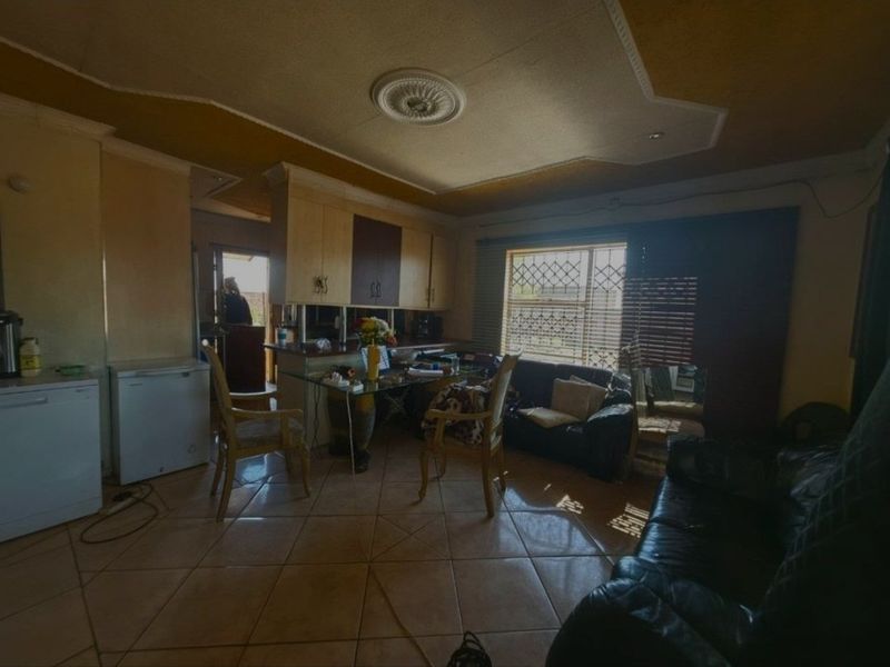 Open-plan living and kitchen area featuring tiled flooring, built-in cabinetry, and decorative ceiling detailing, requiring cosmetic updates to improve the overall aesthetic.