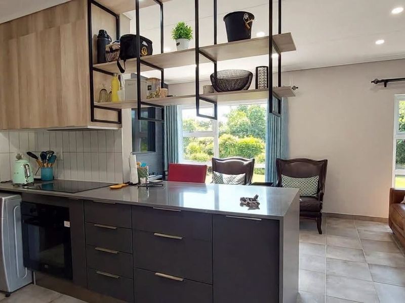 Modern open-plan kitchen and living area featuring a central island, built-in oven, hob, and sleek cabinetry, creating a functional and cohesive living space.
