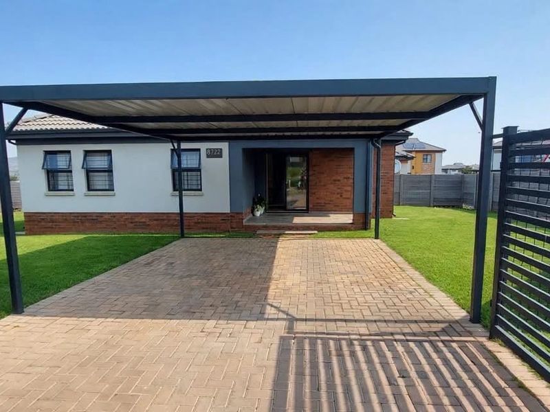 Front view of the property featuring a paved driveway, a modern metal carport, and secure perimeter fencing surrounding the front garden.