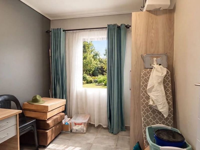 A functional bedroom featuring tiled flooring, a built-in cupboard, and a dark accent wall with natural light from the window.