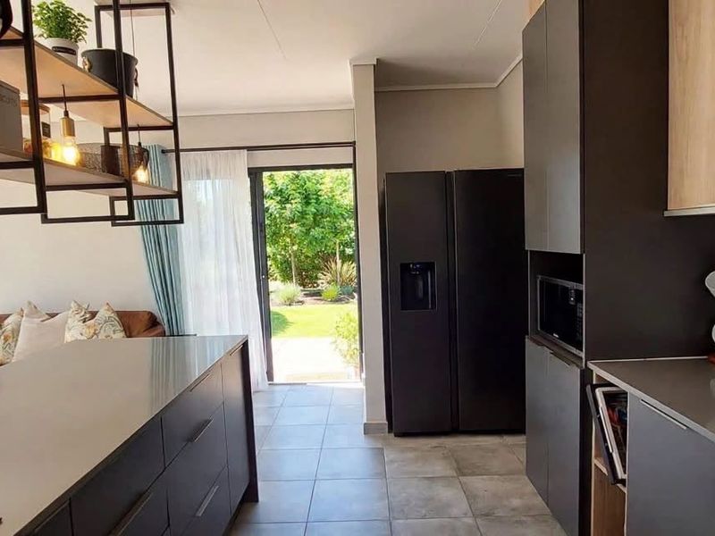 Modern open-plan kitchen and living area featuring sleek cabinetry, stone countertops, a central island, and direct access to the garden through sliding doors.