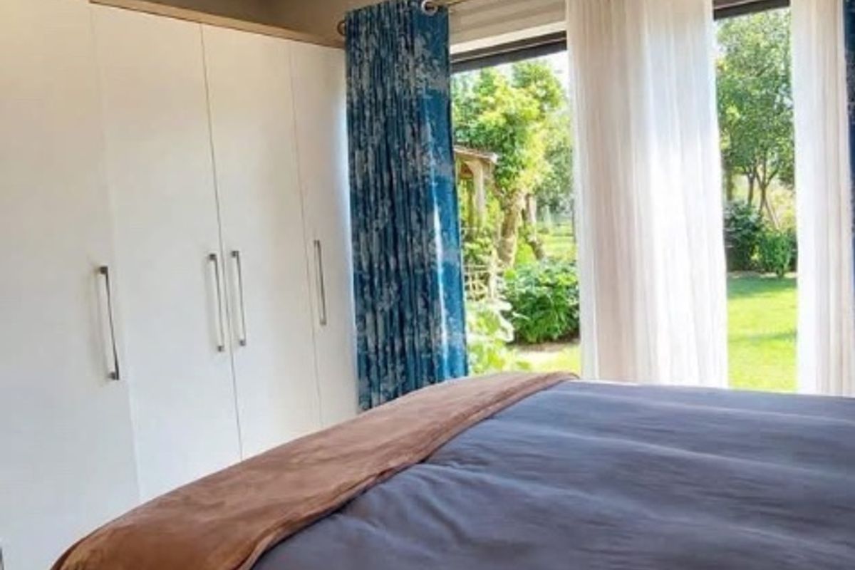 A bright bedroom featuring built-in cupboards, recessed downlighting, and a sliding glass door providing direct access to the garden.