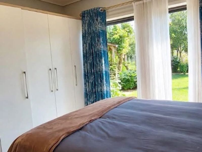 A bright bedroom featuring built-in cupboards, recessed downlighting, and a sliding glass door providing direct access to the garden.