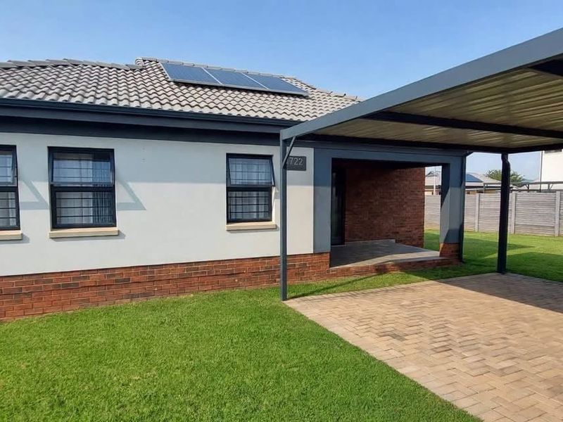 Modern single-story home featuring a tiled roof with solar panels, brick and plaster facade, and a convenient attached carport with paved driveway.