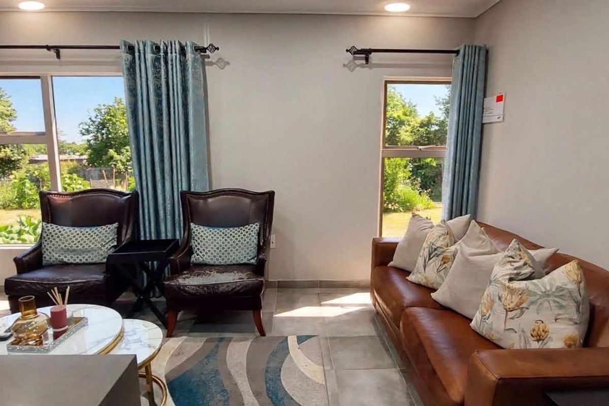 A well-lit living room featuring tiled flooring, recessed downlights, and large windows with garden views.