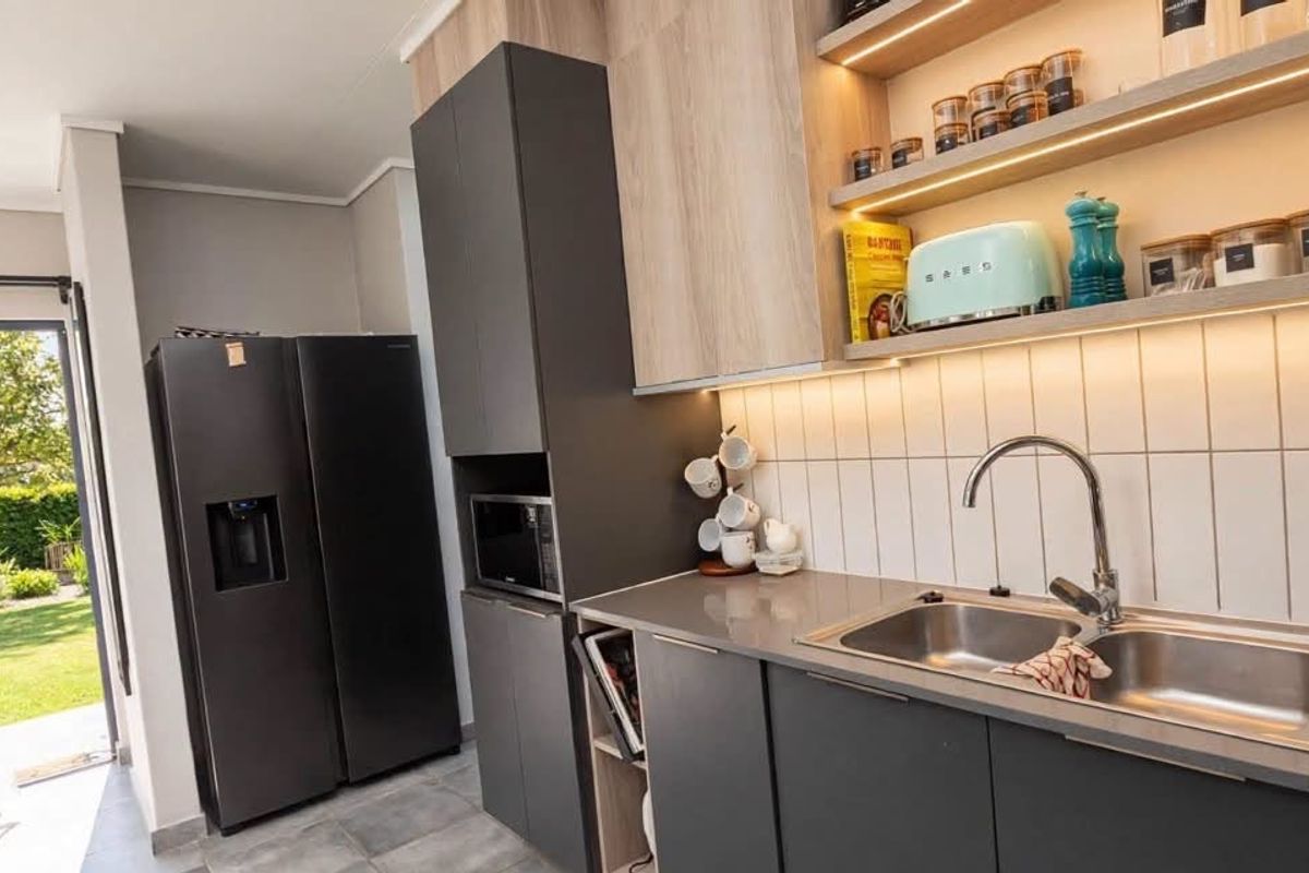 Modern kitchen featuring sleek dark cabinetry, light wood-tone accents, integrated microwave, double stainless steel sink, and stylish tiled backsplash with ambient under-cabinet lighting.