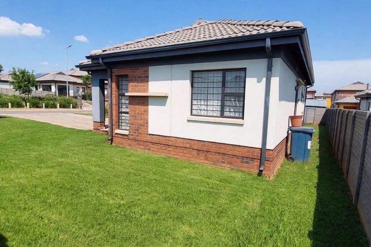 A view of the rear exterior of the apartment, featuring a well-maintained lawn, brick and plastered facade, and secure boundary walls.