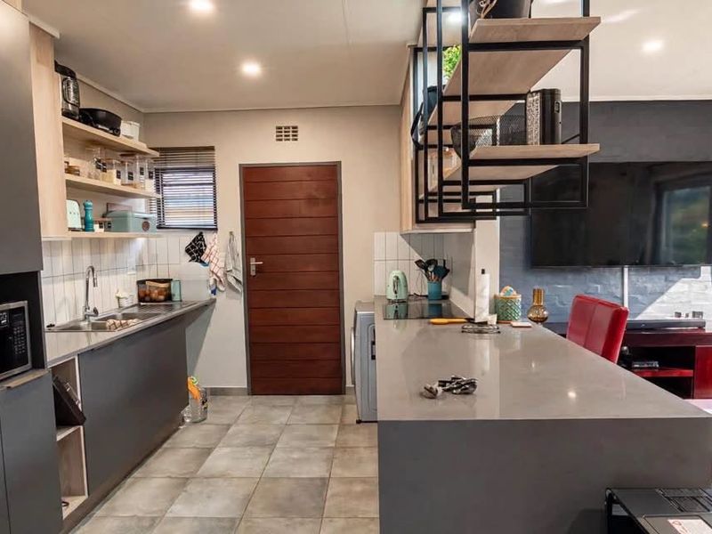 Modern open-plan kitchen and living area featuring sleek dark cabinetry, stone countertops, a central island, and direct access to the outdoor space.