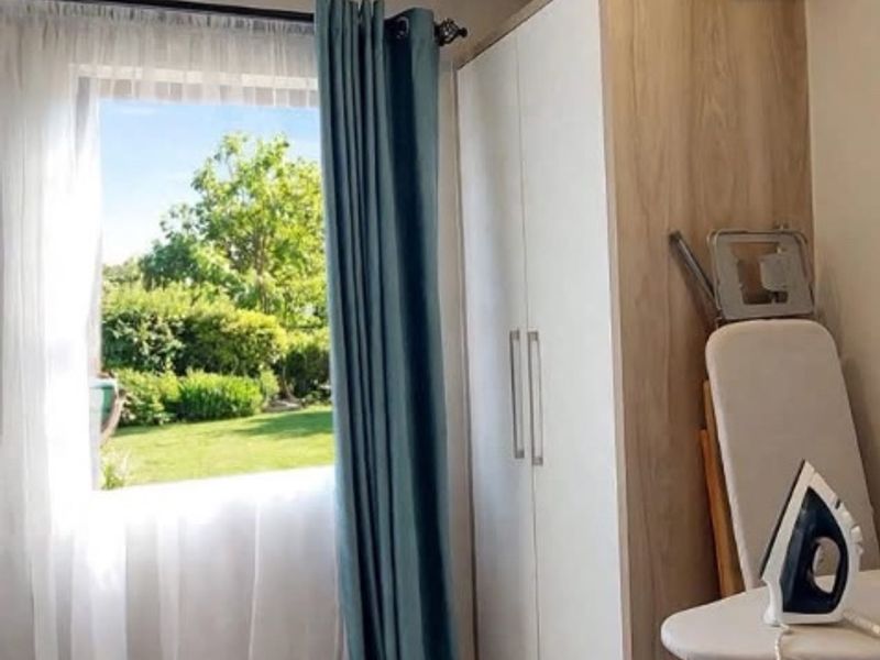 A functional laundry area featuring tiled flooring, a built-in storage cupboard, and a window providing natural light and garden views.