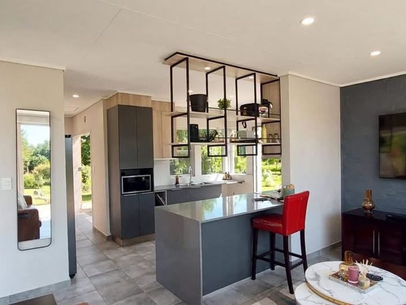 Modern open-plan living area featuring a sleek kitchen with a central island, suspended shelving, and tiled flooring, seamlessly connecting to the living space.