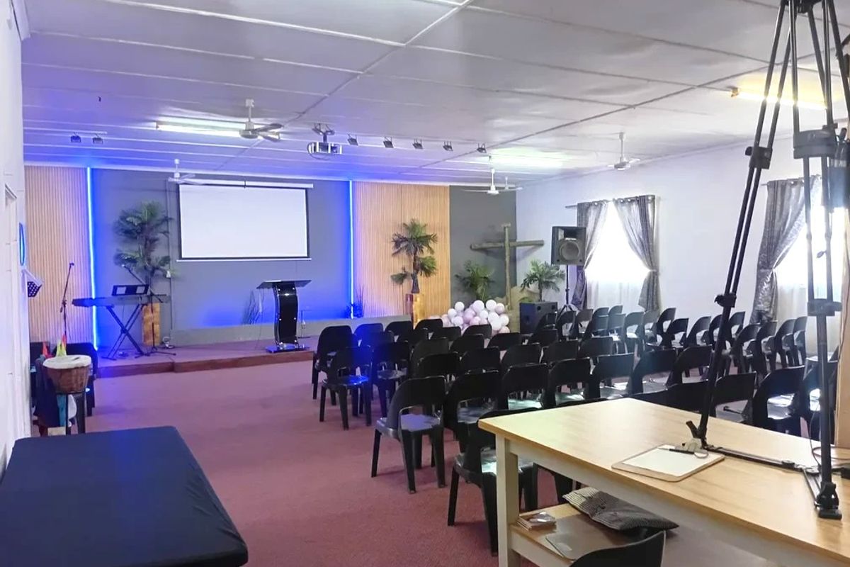 A functional assembly hall or clubhouse space featuring a raised stage, projector screen, and integrated track lighting, suitable for community gatherings or events.